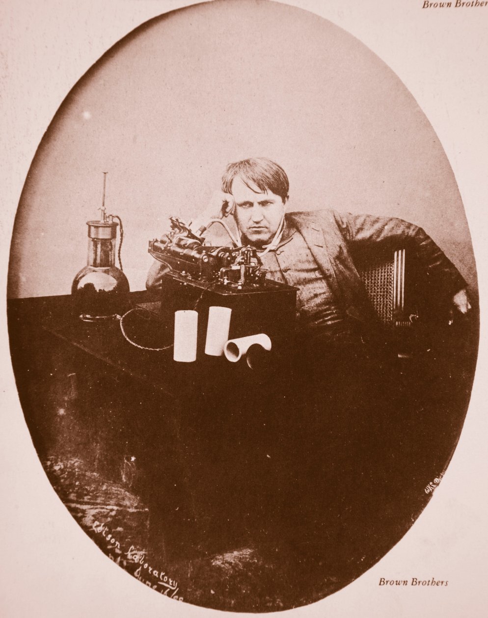 توماس أ.إديسون يجلس بجوار جهازه المحسن ، 1889 (صورة بني داكن) بواسطة مصور أمريكي