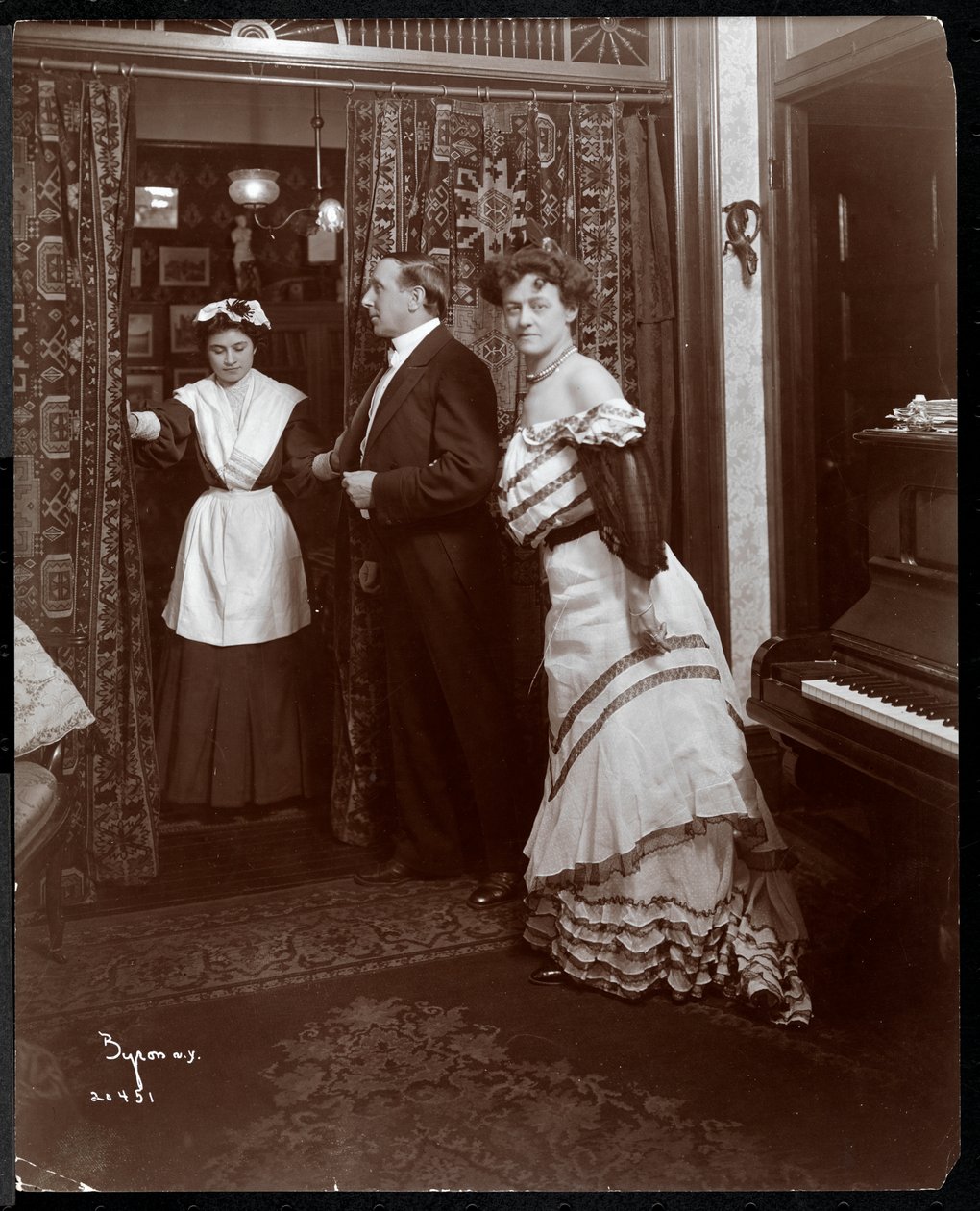 رجل وامرأة يرتدون ملابس رسمية وما يبدو أنه خادم منزلي في غرفة بها بيانو ، 1905 (طباعة الجيلاتين الفضي) بواسطة شركة بايرون