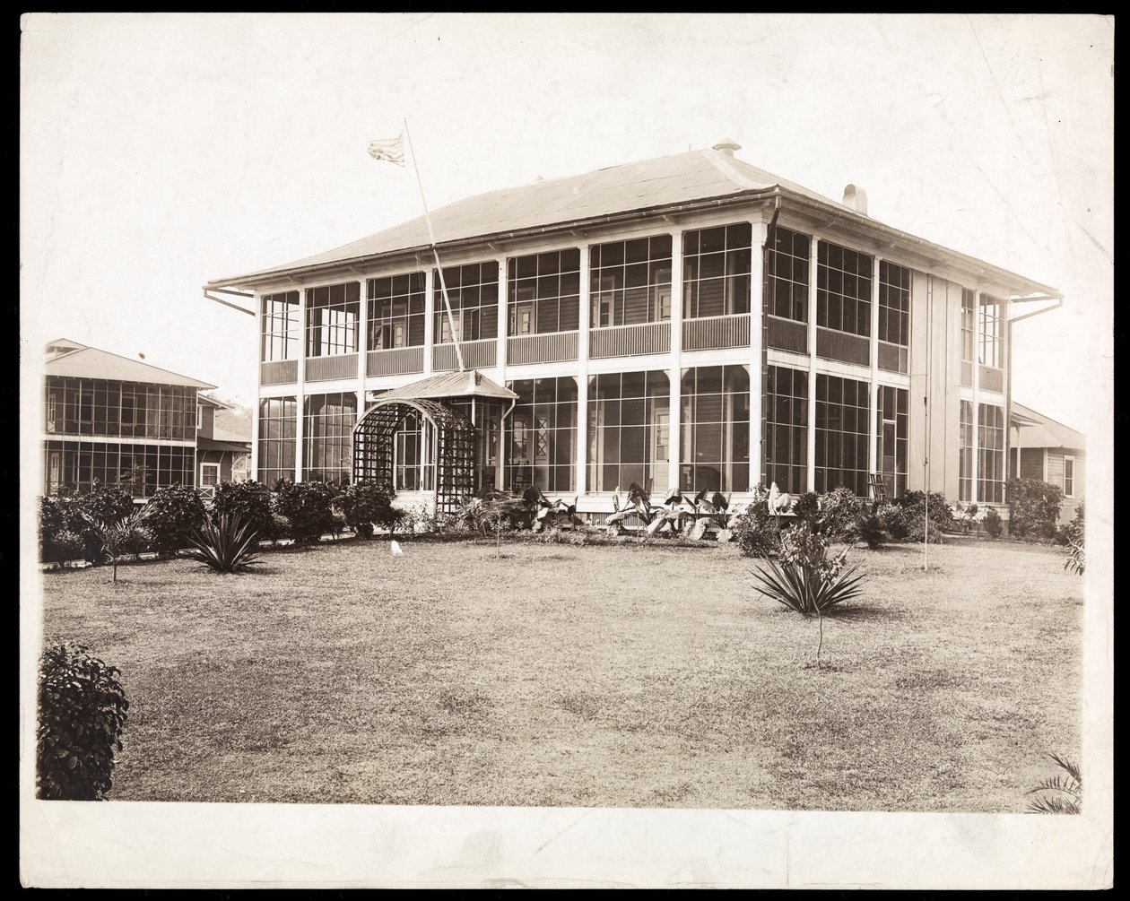 منزل من طابقين محاط بالشرفات ، بعلم أمريكي ؛ في بنما أثناء بناء القناة ، 1912 (طباعة الجيلاتين الفضي) بواسطة شركة بايرون