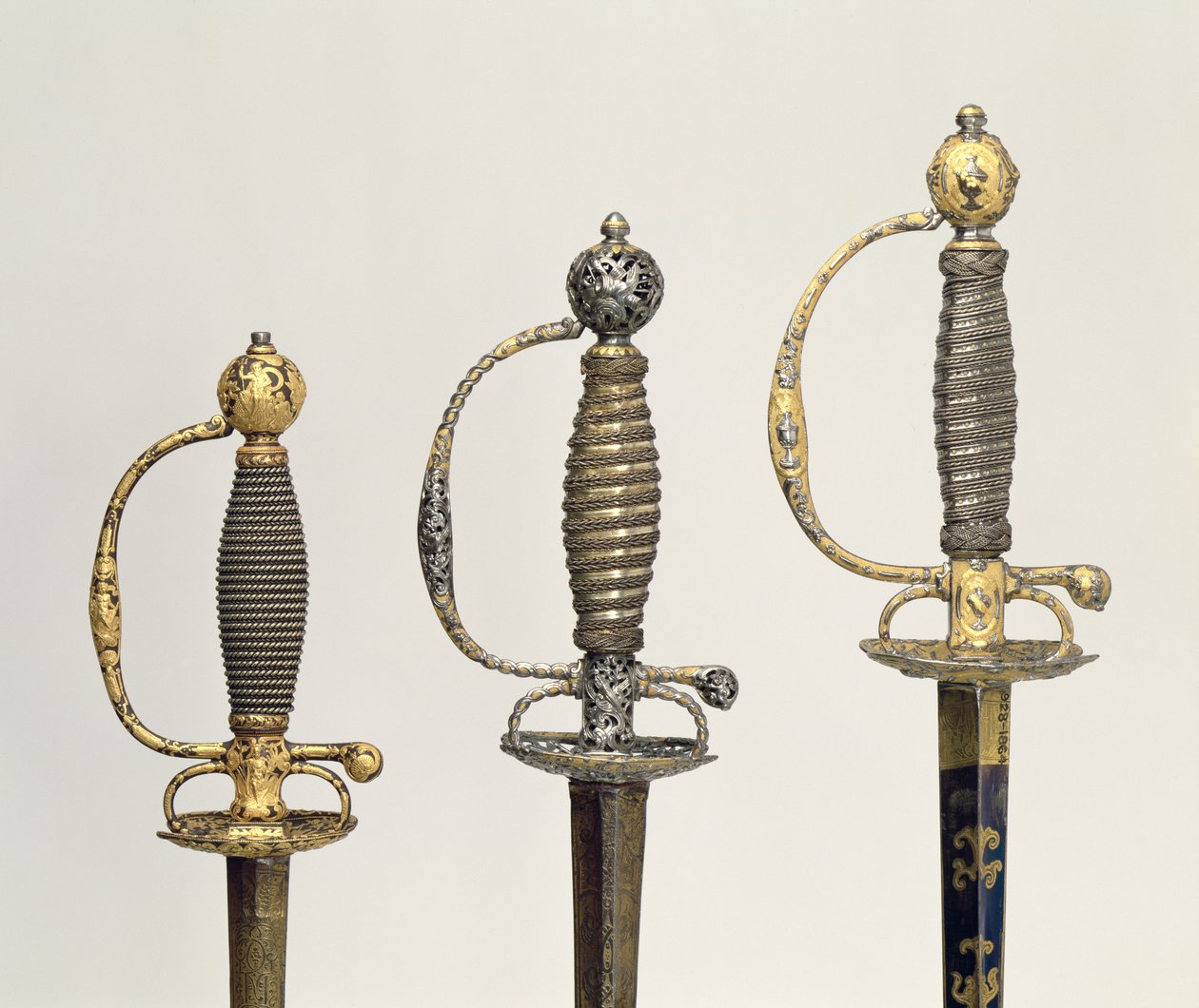 تلال لثلاثة سيوف فرنسية: واحد من الصلب ، أزرق ومغطى بتصاميم من الذهب المطارد ، c.1730 ؛ واحدة من الفولاذ المثقوب والمنقوش وأرضية الذهب المطفأ ، c.1760 ؛ واحدة من الصلب المحفور ، غرام بواسطة غير معروف غير معروف