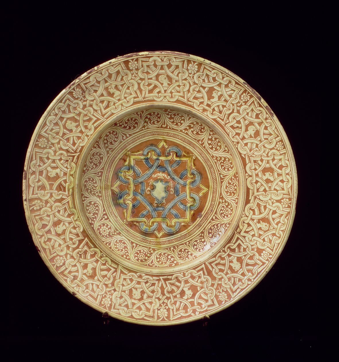 Maiolica plate decorated with an elaborate repetitive knot design framing profile heads on the border and a shield in the central plaque, Italian, made in Tuscany بواسطة غير معروف