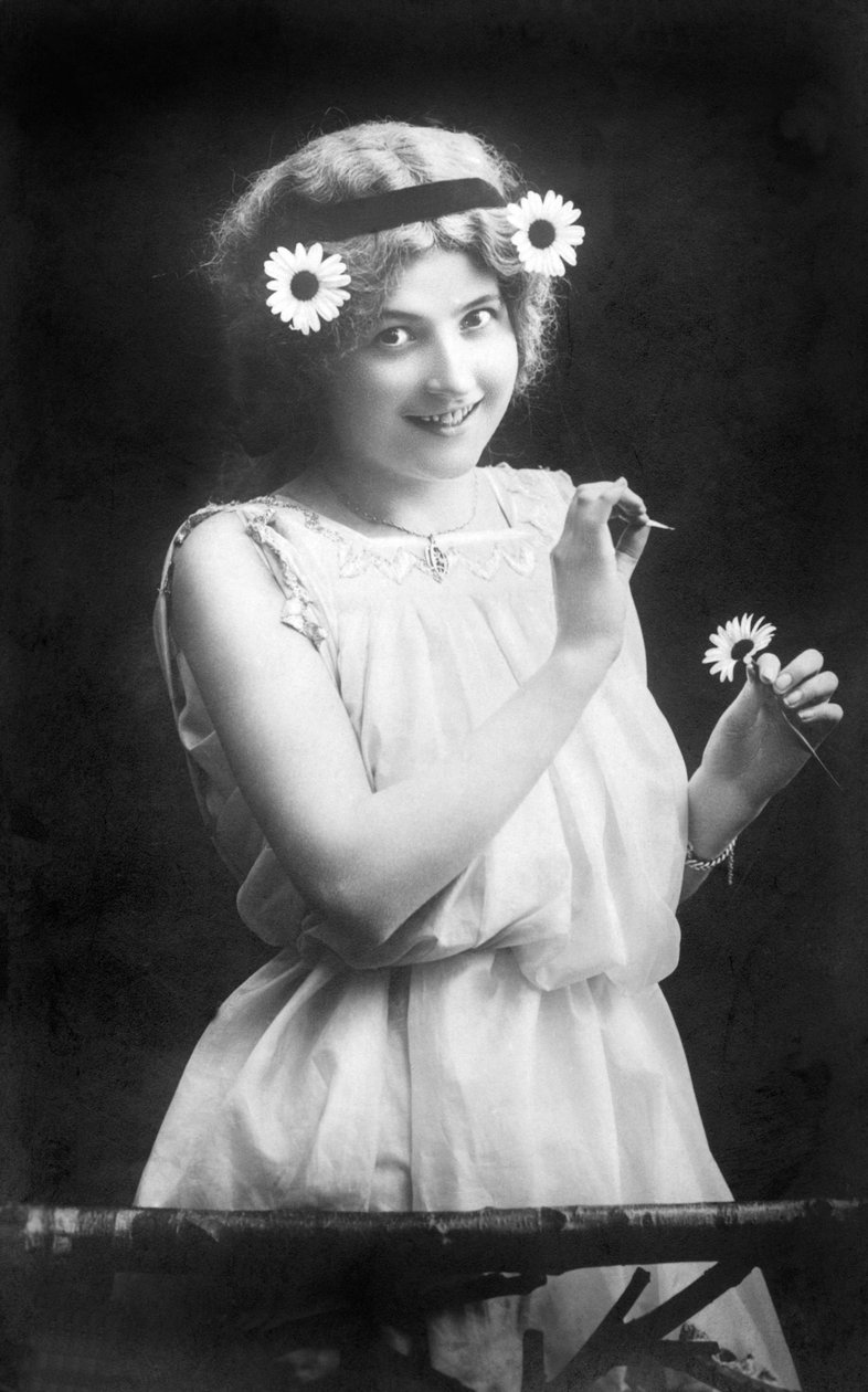 امرأة تسحب بتلات من زهرة: "" يحبني. لا يحبني. إنه يحبني ... "التصوير الفوتوغرافي حوالي عام 1912 بواسطة غير معروف