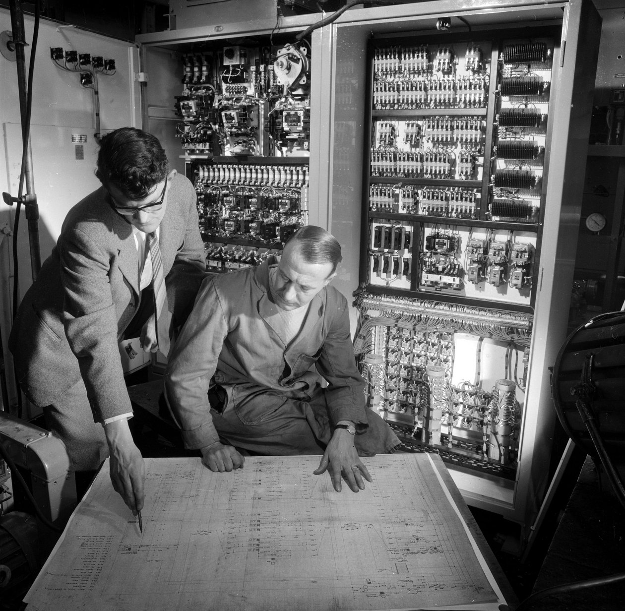 Engineers discuss plans in front of the electronic control panel they have built بواسطة فريدريك (المرتبط ب) بارنارد