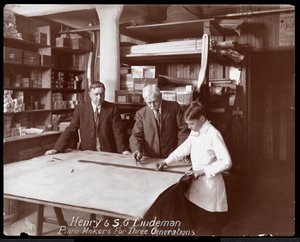 صورة لهنري و SG Lindeman مع ابنهما أو حفيدهما فوق رسومات متجر للبيانو ، 1910 (طباعة الجيلاتين الفضي)