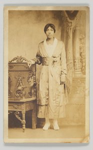 بطاقة بريدية فوتوغرافية لسيدة تقف بجانب كرسي خشبي ، 1904-1918. بواسطة غير معروف