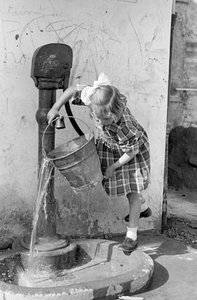 فتاة صغيرة تفرغ دلوًا من الماء في نافورة مضخة، 9 مايو 1939 (صورة بالأبيض والأسود)