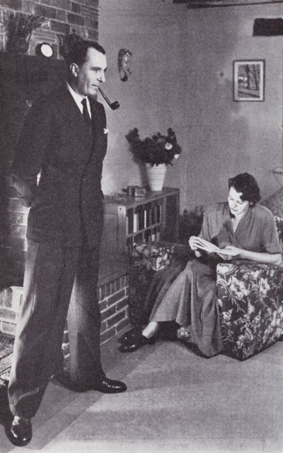 الزوجة تقرأ ، والزوج يدفئ ظهره ضد النار حوالي عام 1950 بواسطة مصور انجليزى