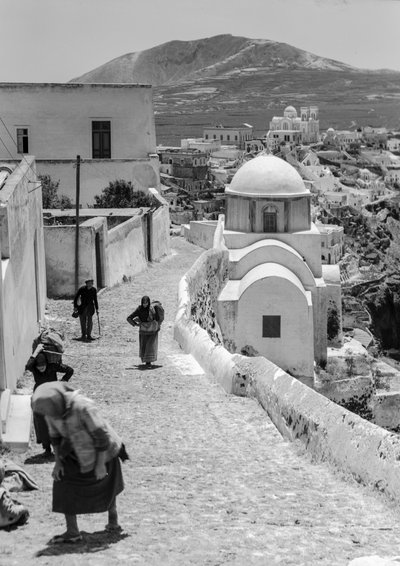 سكان قرية يونانية يسيرون في طريق مرصوف بالحصى في قرية يونانية ذات بناء أبيض... بواسطة ماينارد أوين ويليامز