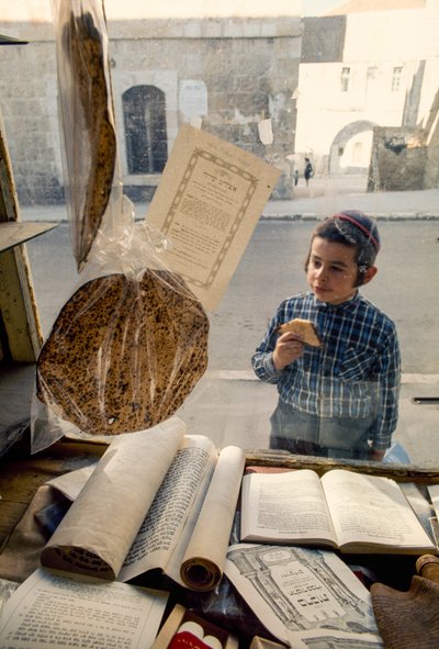 صبي يهودي محافظ يأكل الكعك وهو ينظر إلى مكتبة الكتب الدينية. بواسطة تيد شبيغل
