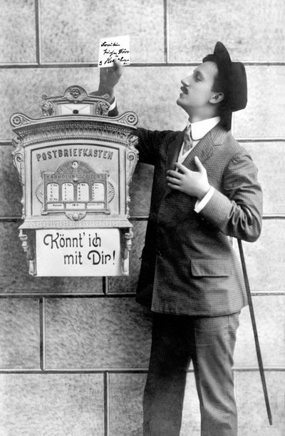 رجل أنيق يرتدي بدلة وقبعة وعصا ، ينشر ملاحظة في صندوق بريد. ألمانيا حوالي عام 1920 ، صورة تاريخية ، رجل بجوار صندوق بريد ، حوالي عام 1920 بواسطة غير معروف