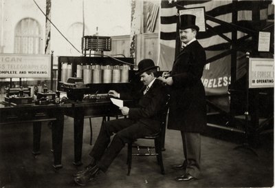 Lee DeForest (جالسًا) يرسل رسالة هاتفية لاسلكية في قسم الكهرباء في معرض 1904 العالمي بواسطة غير معروف