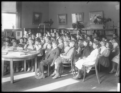أطفال جالسون ، يستمعون في غرفة القراءة في فرع مجهول من مكتبة Queens Borough العامة ، ج .1910 بواسطة وليام ديفيس هاسلر