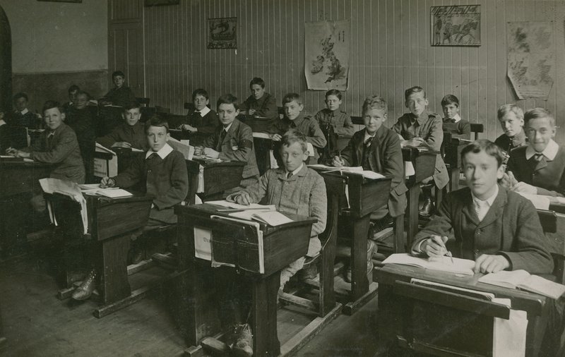 التلاميذ الذكور يجلسون خلف مكاتبهم خلال درس في المدرسة بواسطة مصور انجليزى